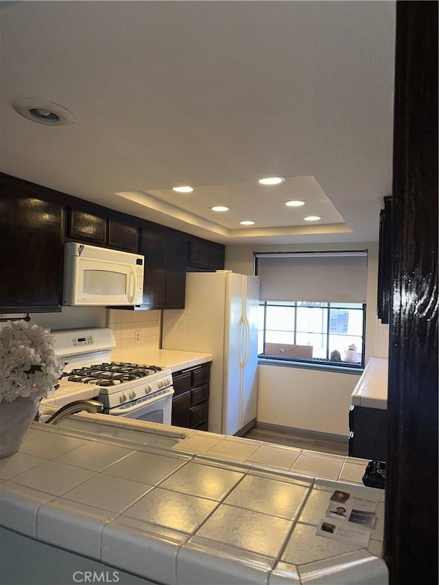 kitchen with tile counters, a tray ceiling, white appliances, and recessed lighting