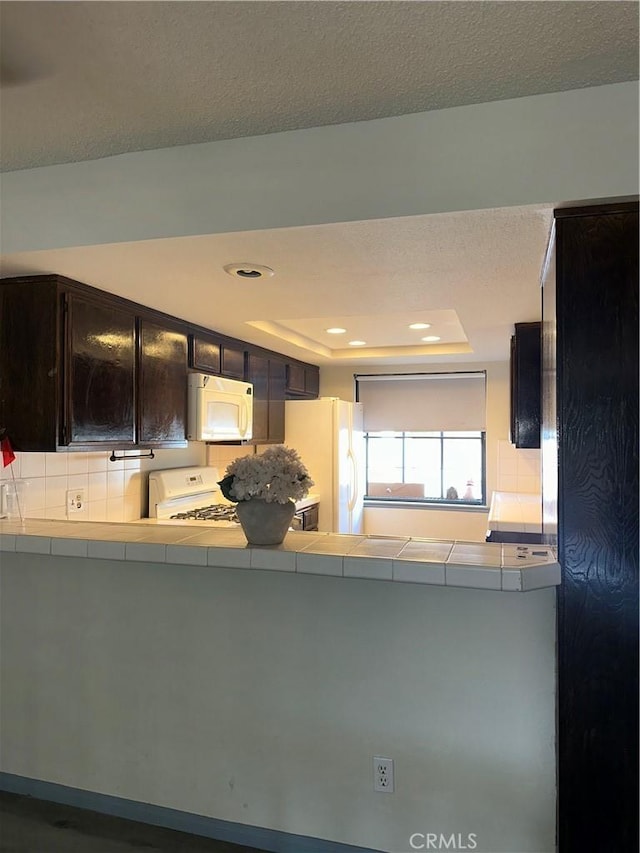 kitchen with white appliances, a raised ceiling, tile countertops, and a textured ceiling