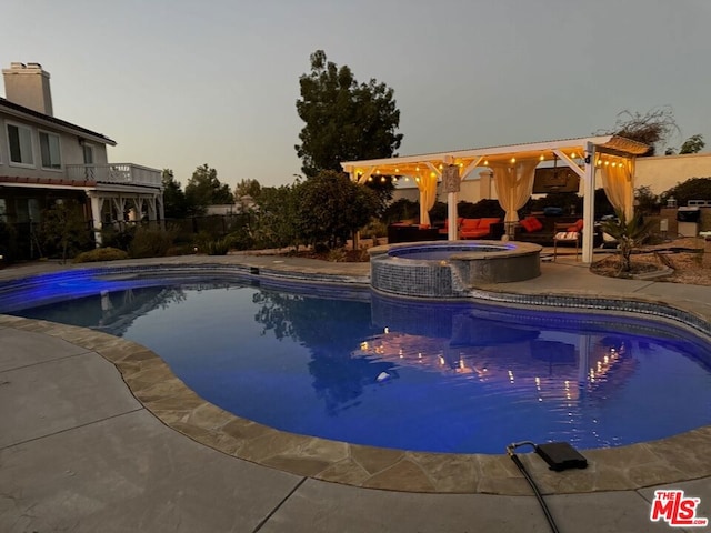 pool at dusk with an in ground hot tub and a patio area