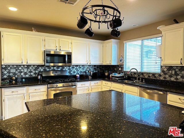 kitchen featuring appliances with stainless steel finishes, hanging light fixtures, white cabinets, backsplash, and sink