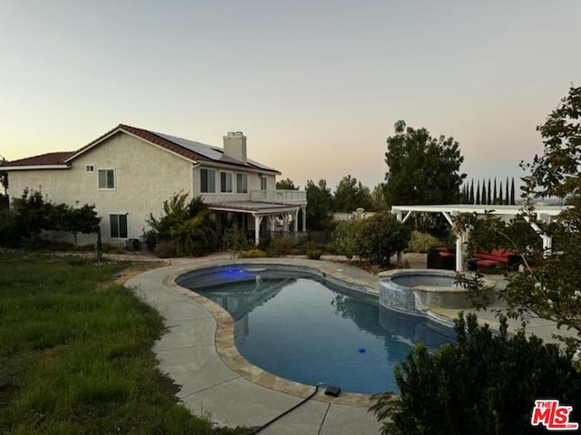 pool at dusk featuring an in ground hot tub