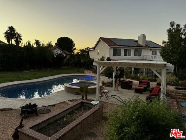 pool at dusk featuring a patio and an in ground hot tub