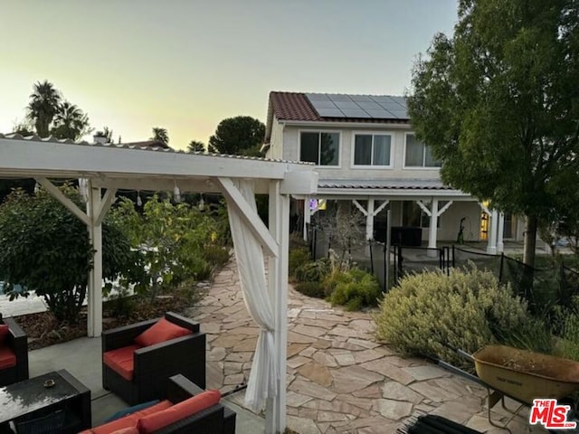 back house at dusk with an outdoor living space, solar panels, and a patio area