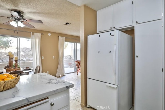 kitchen featuring white cabinets, light stone counters, white fridge, and a textured ceiling