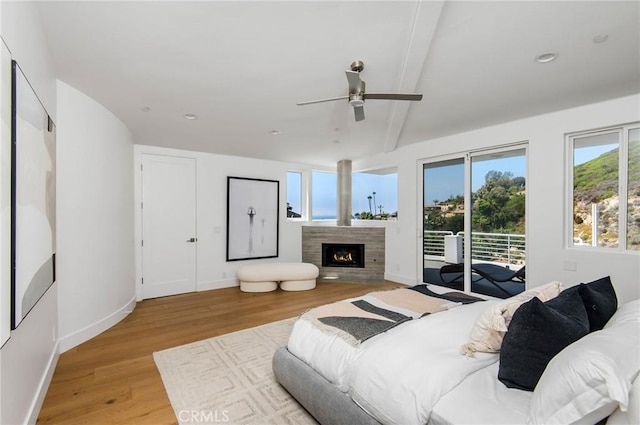 bedroom with a warm lit fireplace, light wood-style flooring, baseboards, beam ceiling, and access to exterior