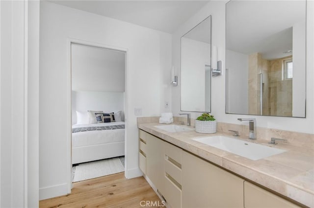 ensuite bathroom featuring wood finished floors, a sink, double vanity, and a tile shower