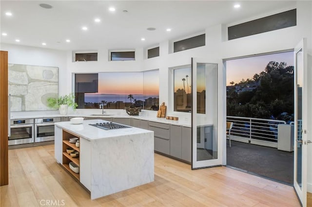 kitchen with gray cabinetry, appliances with stainless steel finishes, light wood-type flooring, a center island, and sink