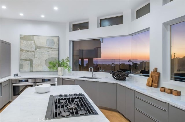 kitchen featuring stainless steel oven, gray cabinets, black gas stovetop, and a sink