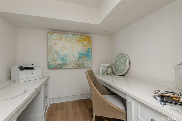 home office featuring light wood finished floors, built in desk, and baseboards