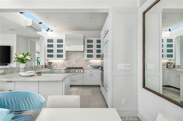 kitchen with white cabinets, appliances with stainless steel finishes, a peninsula, an AC wall unit, and wall chimney range hood