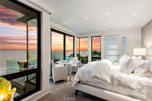 bedroom with wood finished floors, a water view, access to outside, expansive windows, and recessed lighting