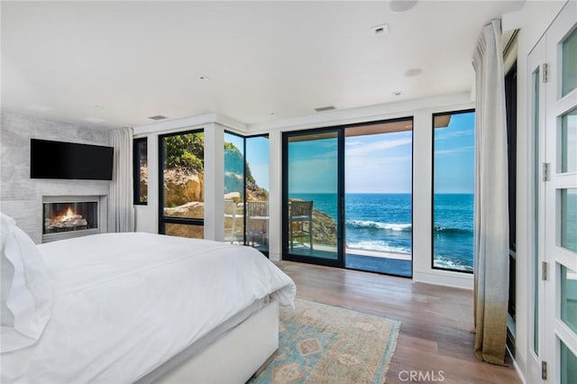 bedroom with a large fireplace, wood finished floors, a water view, access to exterior, and floor to ceiling windows