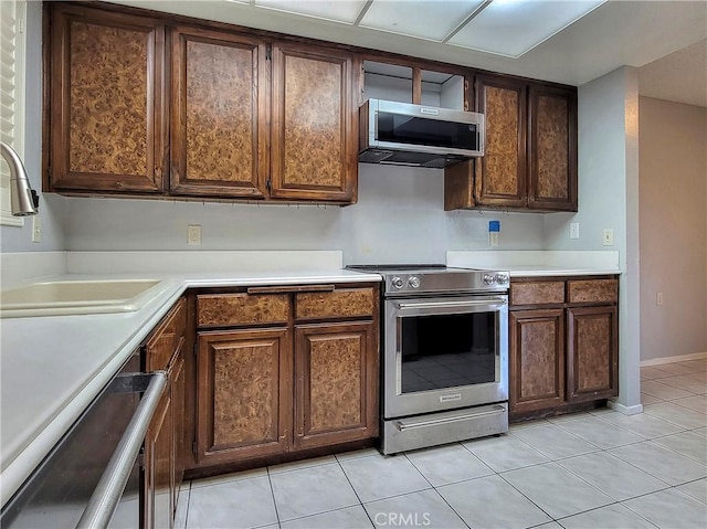 kitchen featuring dark brown cabinets, sink, stainless steel appliances, and light tile patterned flooring