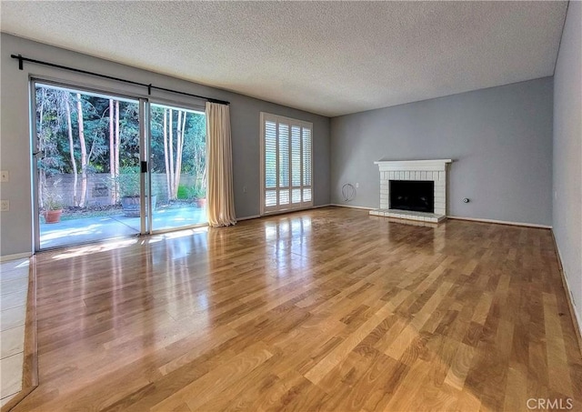 unfurnished living room featuring a brick fireplace, a textured ceiling, and light hardwood / wood-style flooring