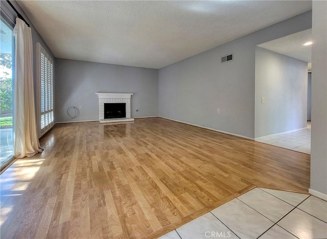 unfurnished living room featuring a fireplace, light hardwood / wood-style flooring, and a textured ceiling