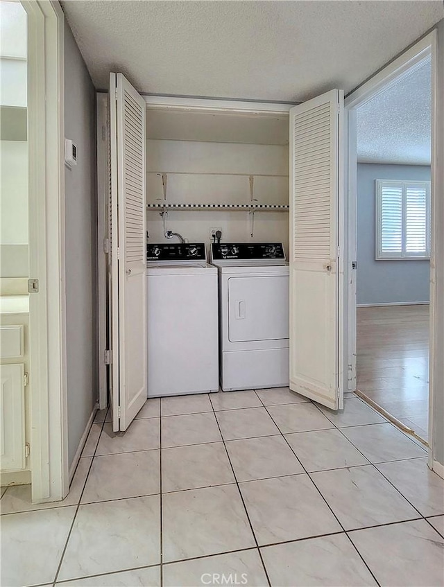 laundry room featuring washer and clothes dryer, light tile patterned floors, and a textured ceiling