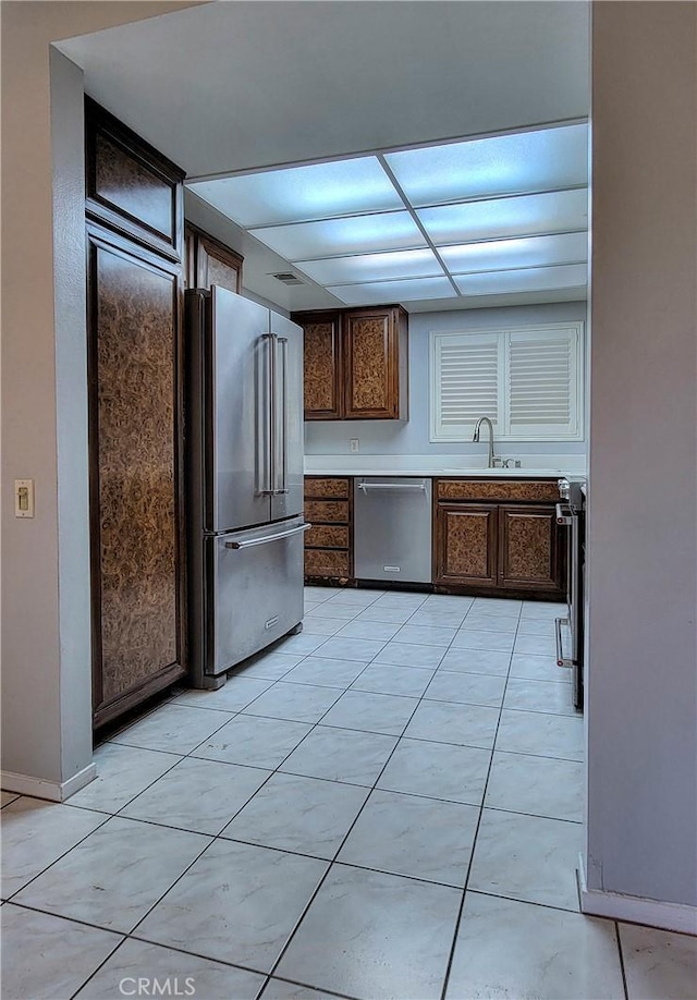 kitchen with a drop ceiling, sink, light tile patterned floors, dark brown cabinetry, and stainless steel appliances