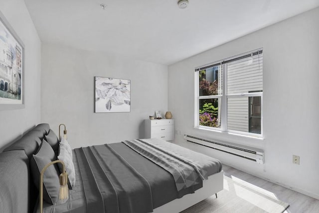 bedroom with light hardwood / wood-style floors and a baseboard heating unit