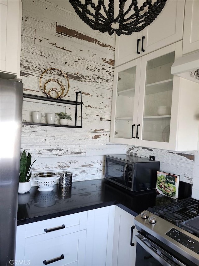 kitchen featuring stainless steel range with gas cooktop, white cabinets, and wooden walls