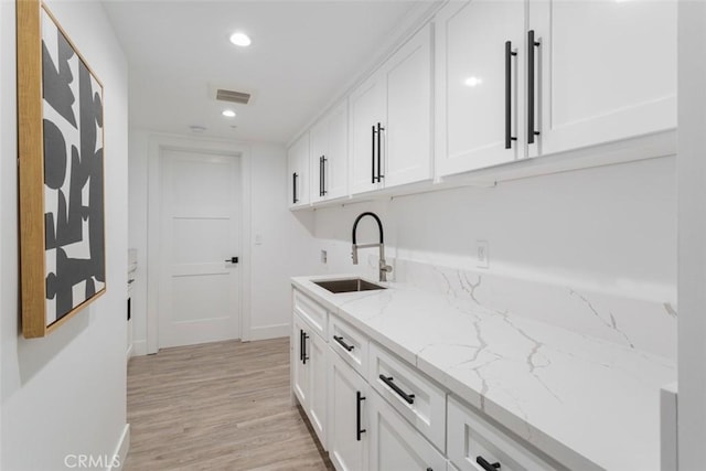 kitchen featuring light stone counters, sink, white cabinets, and light wood-type flooring