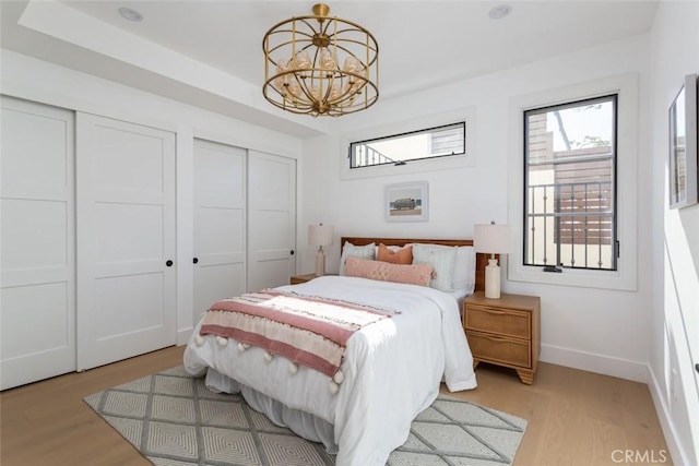 bedroom with two closets, an inviting chandelier, and light hardwood / wood-style flooring