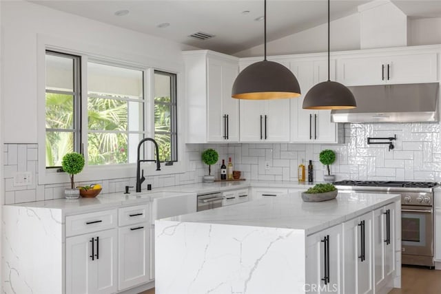 kitchen featuring light stone countertops, stainless steel range, vaulted ceiling, white cabinetry, and range hood