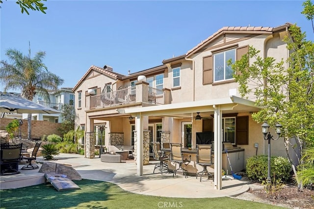 back of property with an outdoor living space, a balcony, ceiling fan, and a patio area