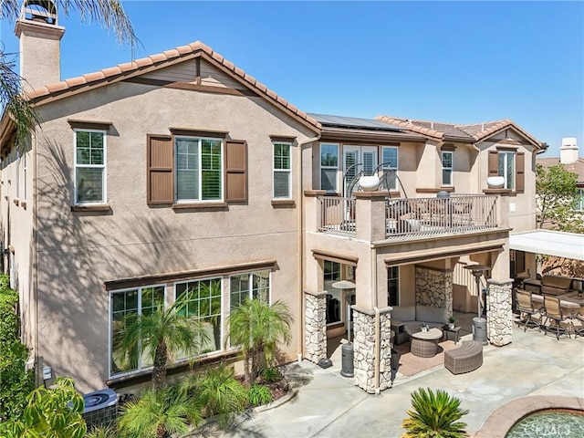 back of property featuring solar panels, cooling unit, an outdoor hangout area, a balcony, and a patio