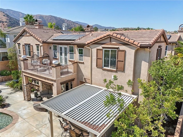 back of property with a balcony, a mountain view, a patio area, and solar panels