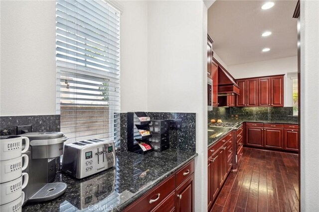 kitchen featuring backsplash, dark hardwood / wood-style floors, stainless steel gas stovetop, and dark stone countertops