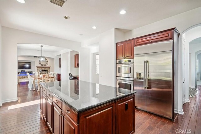 kitchen with a center island, dark stone counters, dark hardwood / wood-style floors, pendant lighting, and stainless steel appliances