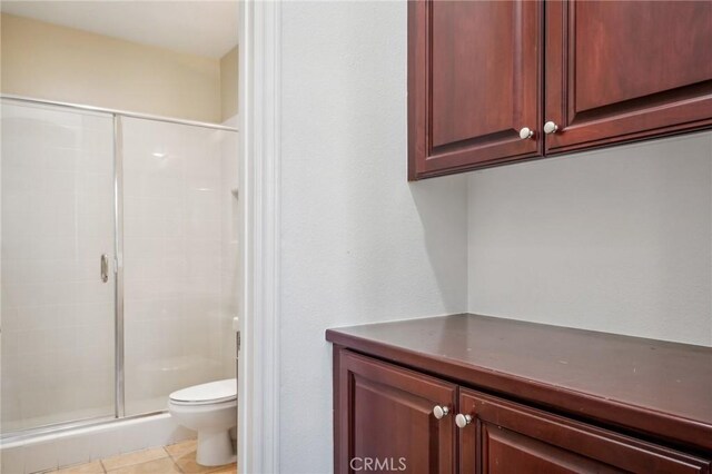 bathroom featuring tile patterned floors, toilet, and a shower with door