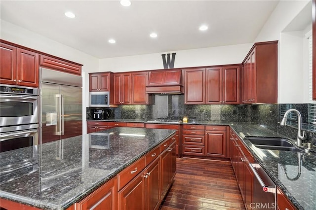 kitchen featuring sink, dark stone countertops, a kitchen island, custom range hood, and stainless steel appliances