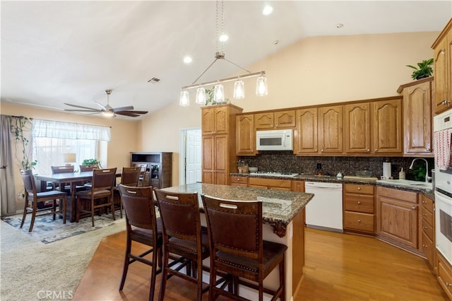 kitchen with tasteful backsplash, white appliances, a center island, light wood-type flooring, and vaulted ceiling