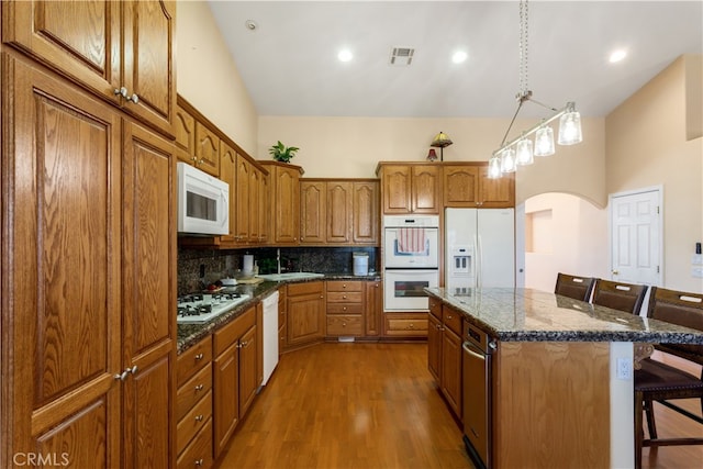 kitchen featuring pendant lighting, wood-type flooring, a kitchen bar, a kitchen island, and white appliances