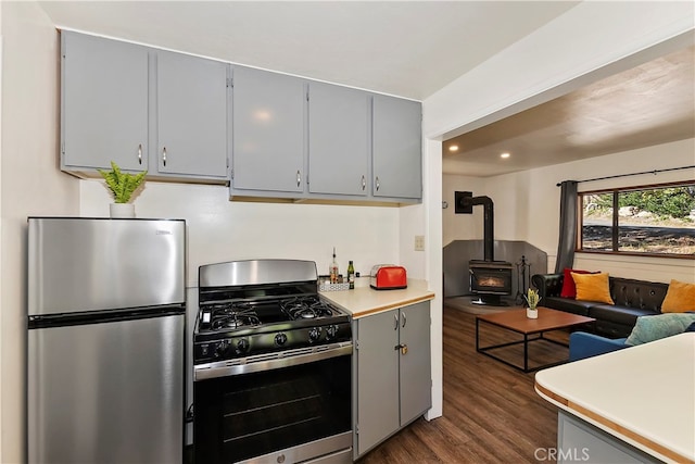 kitchen featuring gray cabinets, appliances with stainless steel finishes, dark wood-type flooring, and a wood stove