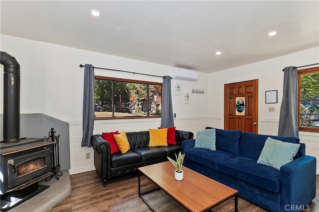 living room with wood-type flooring, plenty of natural light, a wood stove, and a wall mounted AC