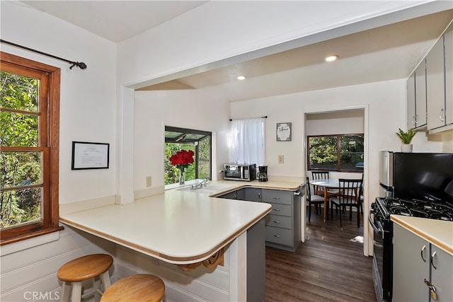 kitchen featuring range with gas stovetop, kitchen peninsula, gray cabinetry, a kitchen bar, and a wealth of natural light