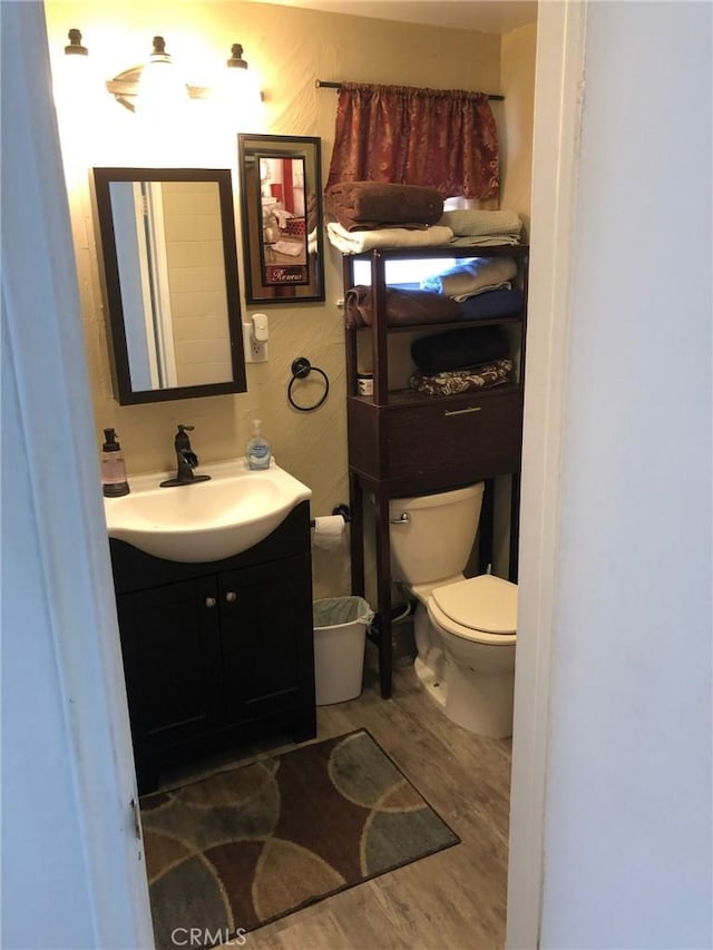 half bath featuring toilet, wood finished floors, and vanity