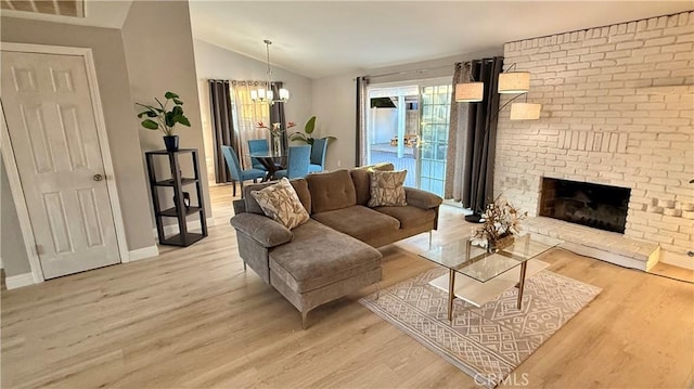 living room featuring a notable chandelier, vaulted ceiling, a brick fireplace, and light wood-type flooring