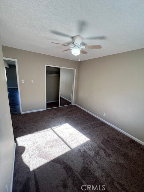 unfurnished bedroom with ceiling fan, a textured ceiling, a closet, and dark carpet