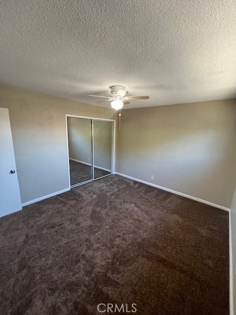 unfurnished bedroom featuring ceiling fan, a textured ceiling, a closet, and dark carpet