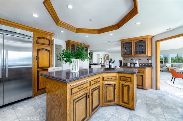 kitchen featuring a center island, tasteful backsplash, built in refrigerator, a raised ceiling, and crown molding