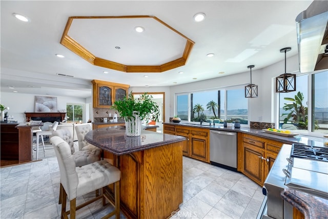 kitchen featuring a tray ceiling, dishwasher, a kitchen bar, decorative light fixtures, and a large fireplace