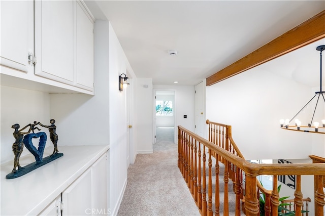 hallway with an inviting chandelier and light colored carpet