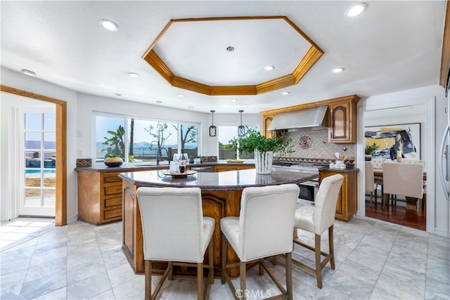 kitchen featuring a kitchen island, decorative light fixtures, wall chimney exhaust hood, crown molding, and decorative backsplash