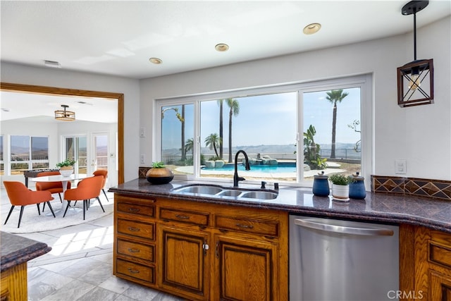 kitchen with dark stone counters, dishwasher, decorative light fixtures, and sink