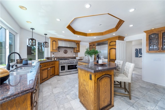 kitchen featuring high end appliances, pendant lighting, a center island, sink, and wall chimney range hood