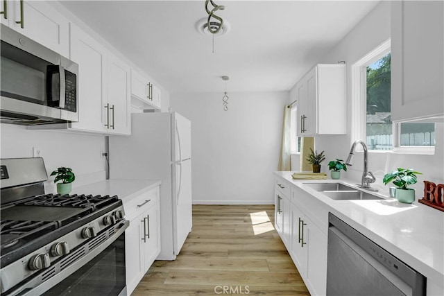 kitchen featuring white cabinets, stainless steel appliances, light hardwood / wood-style floors, sink, and hanging light fixtures