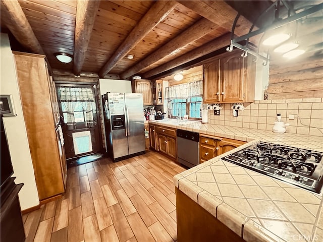 kitchen with beam ceiling, backsplash, stainless steel appliances, tile countertops, and light wood-type flooring